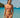 Woman in a pink bikini standing on a beach with clear blue water and a sailboat in the background.