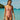 Woman in a pink swimsuit standing in clear blue water with a boat and lush greenery in the background.