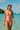 Woman in a pink swimsuit standing in clear blue water with a boat and lush greenery in the background.