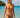Woman in a red bikini standing in clear blue water with a boat and island in the background.