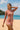 Woman wearing a pink long-sleeve rash guard and patterned shorts on a beach.