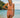 Woman in a pink swimsuit standing on a beach with a clear blue sky and ocean in the background.