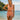 Woman in a pink swimsuit standing on a beach with a clear blue sky and ocean in the background.