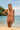 Woman in a pink swimsuit standing on a beach with a clear blue sky and ocean in the background.