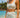 Woman in light blue sports bra and shorts standing on a beach with ocean and sky in the background