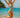 Woman in a green swimsuit jumping on a beach with clear blue water and sky.