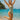 Woman in a green swimsuit jumping on a beach with clear blue water and sky.