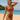 Woman in a rust-colored bikini standing on a beach with ocean and sky in the background
