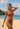 Woman in a rust-colored bikini standing on a beach with ocean and sky in the background