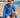 Young boy in a blue patterned swimsuit sitting on a sandy beach.
