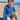 Young boy in a blue patterned swimsuit sitting on a sandy beach.
