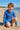 Young boy in a blue patterned swimsuit sitting on a sandy beach.