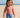 Child wearing a red rash guard and blue swim shorts on a sandy beach.