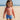 Child wearing a red rash guard and blue swim shorts on a sandy beach.